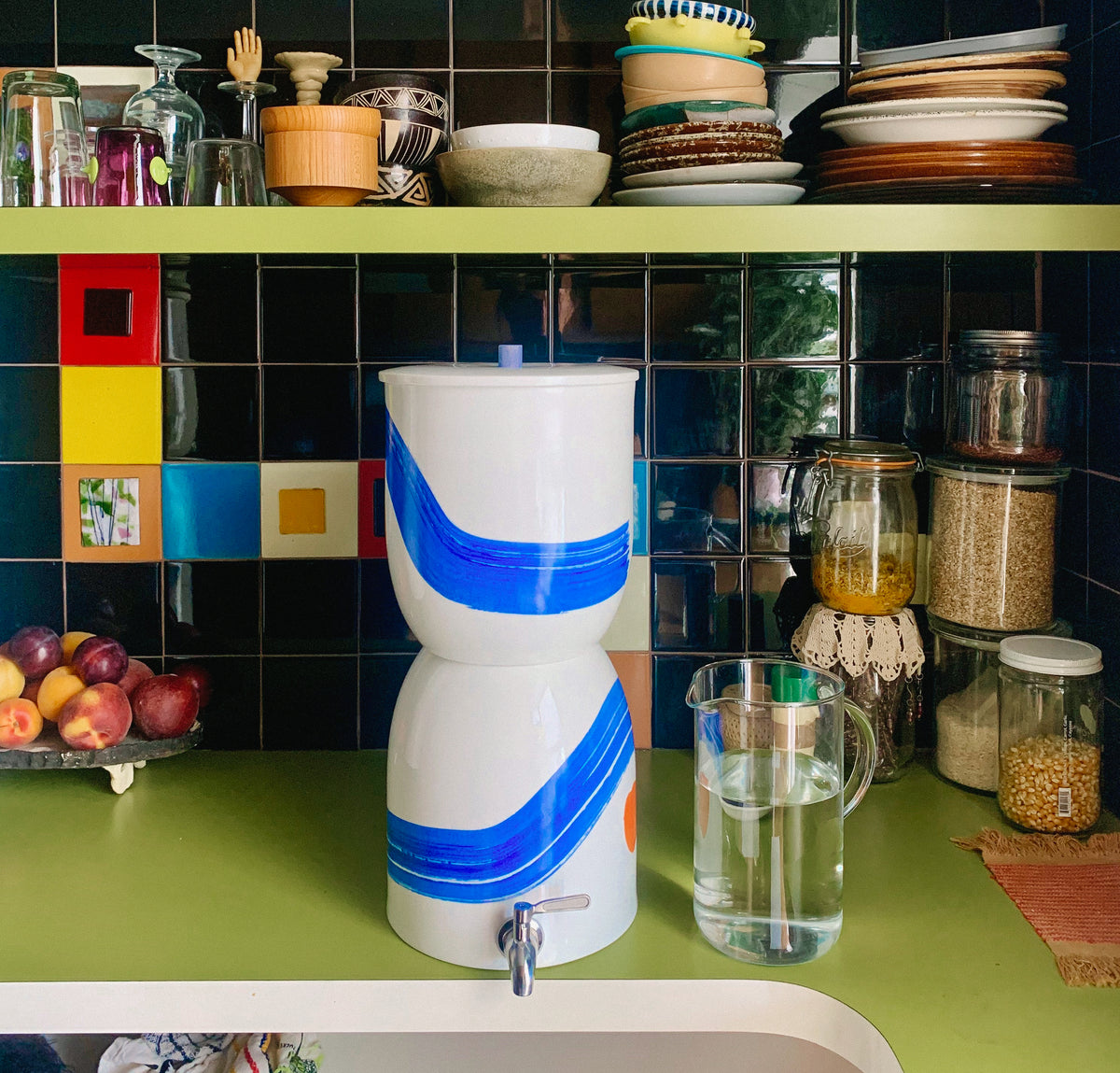 Painted Walter sits on a counter surrounded by tableware and jars